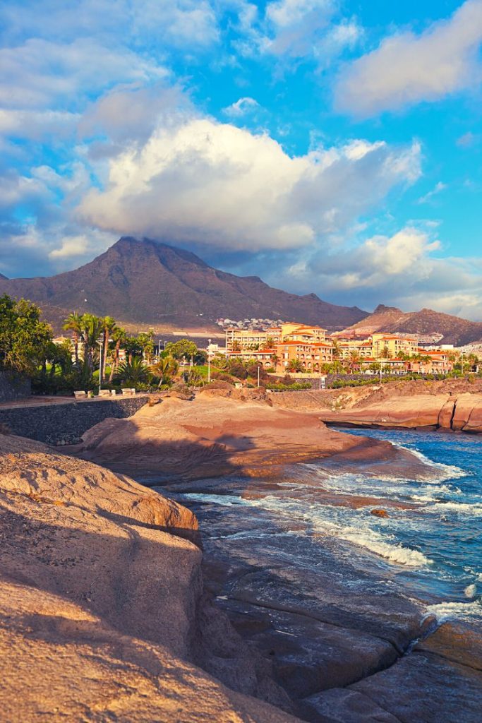 Rocky coastline and scenic mountain view in Tenerife with golden light and calm waves, capturing the island’s perfect climate.