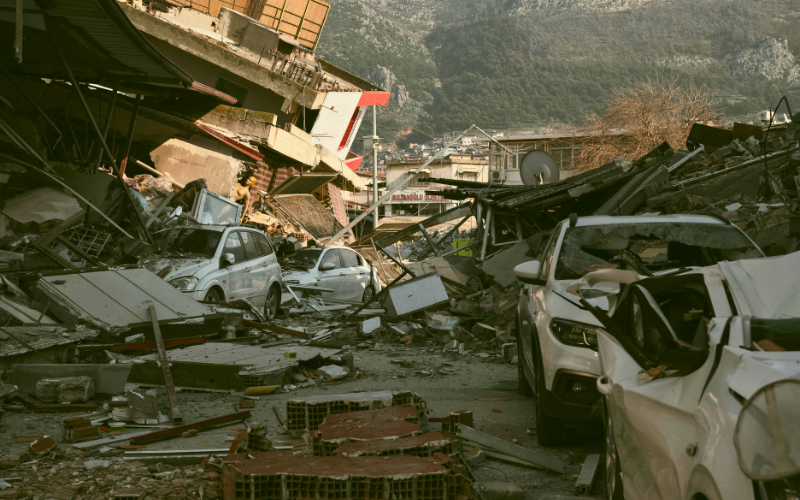 Collapsed buildings and crushed cars after a powerful earthquake, illustrating the devastating impact of natural disasters on urban areas.