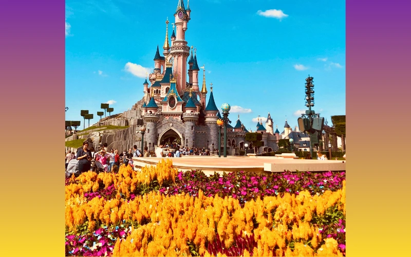 Sleeping Beauty Castle at Disneyland framed by vibrant spring flowers in full bloom under a clear blue sky.