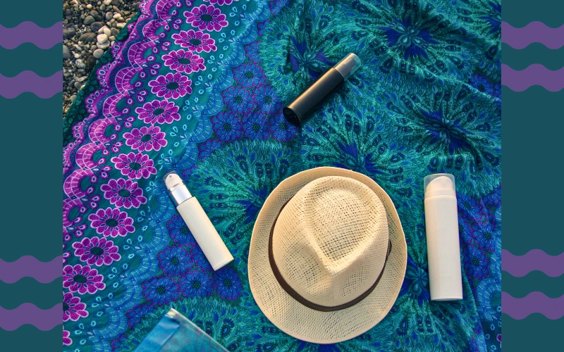 Flat-lay of Disneyland weather essentials including sunscreen, hat, poncho, and water bottle on a colorful cloth.