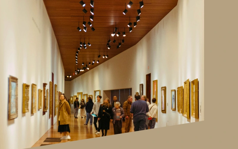 Visitors walking through a Seattle art gallery, observing framed paintings under warm lighting.