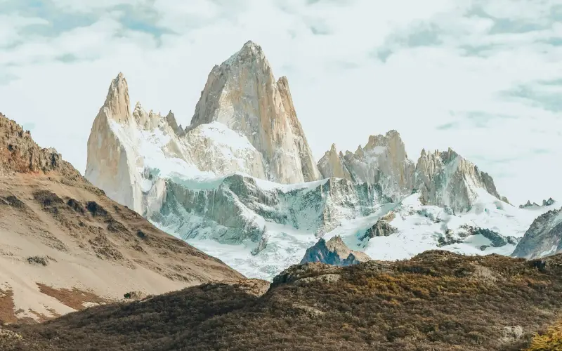 Majestic snow-covered mountain peaks rising above rocky slopes under a clear sky, highlighting the beauty and grandeur of high-altitude glaciers.