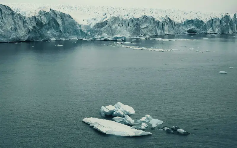 Melting Arctic glacier with floating icebergs in cold ocean water, illustrating the impact of global warming and climate change on polar ice sheets.