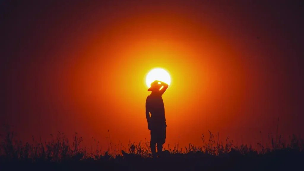 A person stands under the blazing sun during extreme heat, symbolizing the human toll of rising temperatures and increasing global heat-related deaths.