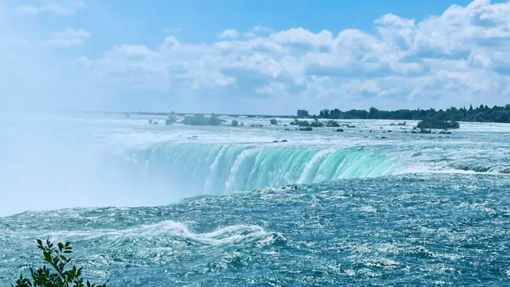 A stunning view of a massive turquoise waterfall cascading into mist under a bright blue sky, capturing the raw power and beauty of Earth’s natural wonders.