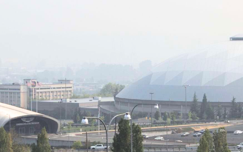 A hazy cityscape with reduced visibility due to wildfire smoke, showing urban buildings and roads under thick atmospheric pollution.
