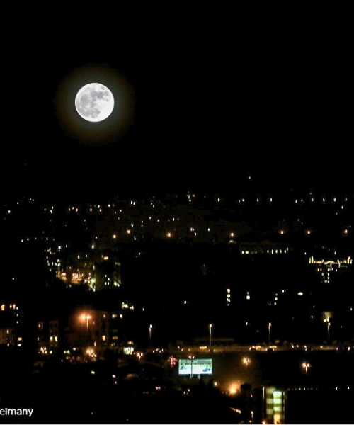 The August 30, 2023 Blue Supermoon glowing brightly above a modern city skyline, appearing slightly larger and brighter than a normal full moon.