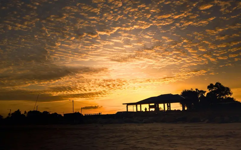 Golden sunset sky with dimmer clouds over a coastal silhouette, linked to reduced air pollution effects