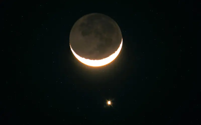 A thin crescent Moon glowing in the night sky with Saturn shining just below it during their close conjunction.