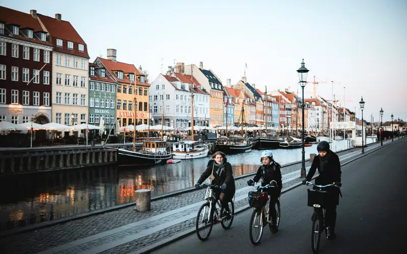 Cyclists riding along the colorful waterfront of Copenhagen, Denmark, showcasing the city’s strong cycling culture and sustainable urban living.