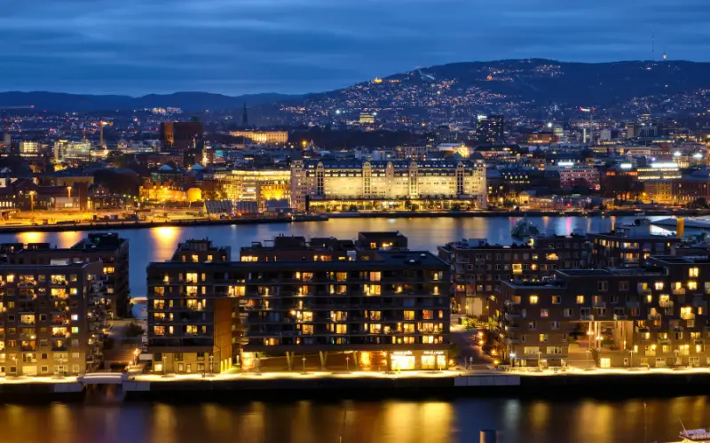 Night view of Oslo, Norway, with illuminated waterfront buildings and surrounding hills, symbolizing the city’s clean energy systems and commitment to sustainable urban living.