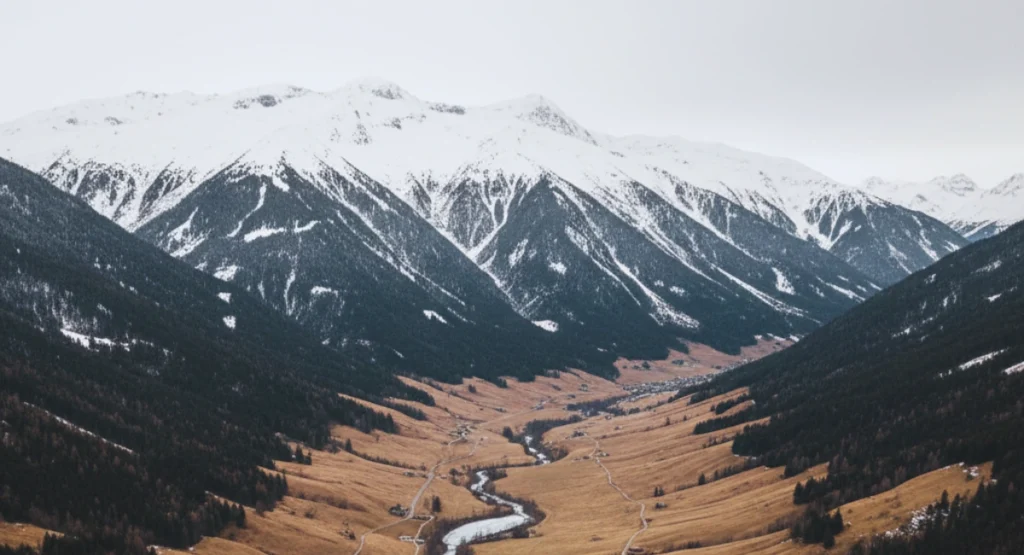 “A wide valley in the European Alps showing snow-covered peaks and mostly snowless brown lower slopes during early winter 2025.”