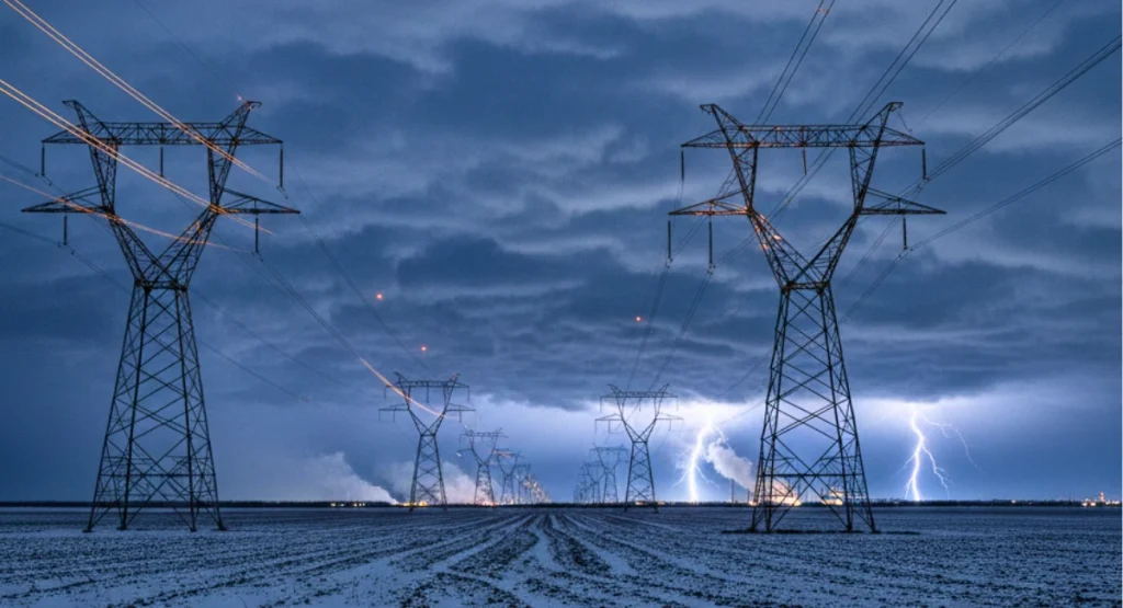 High-voltage power lines stretch across a snowy U.S. landscape as lightning strikes under stormy winter skies, symbolizing the strain on America’s power grid during extreme weather.