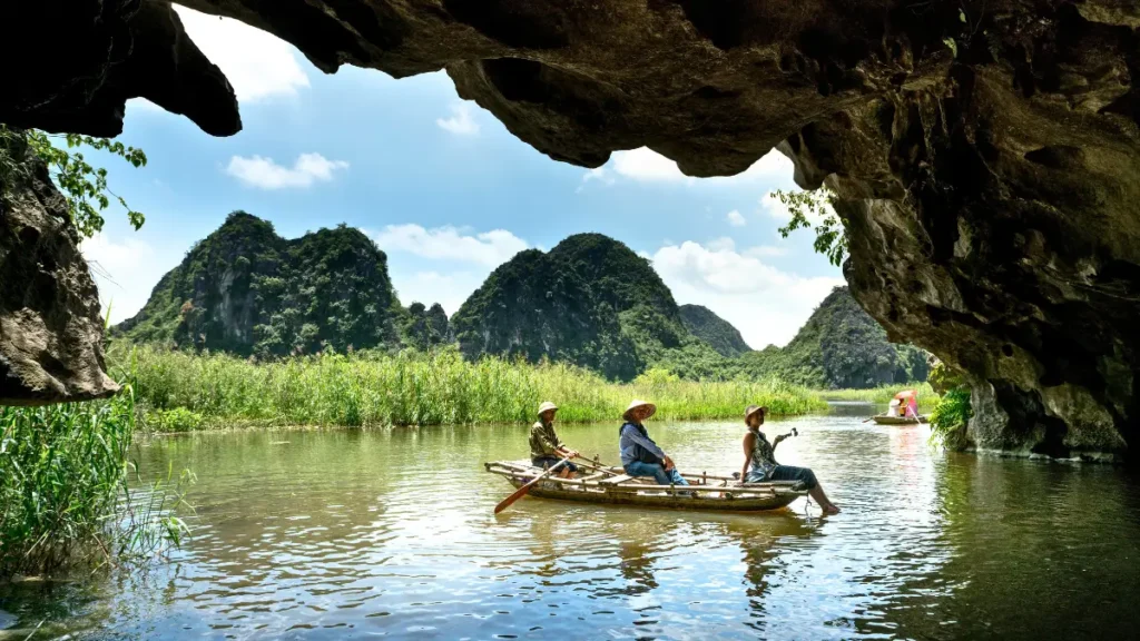 Boat entering a limestone cave in Vietnam with lush mountains in the background.