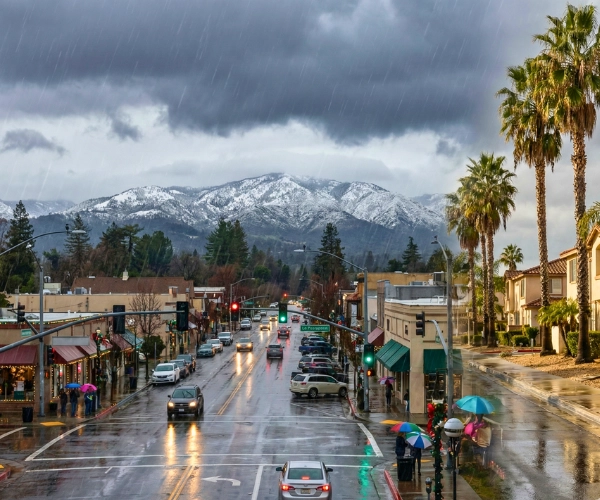 Rainy California town with umbrellas in the foreground and snow-covered mountains in the distance during Christmas week